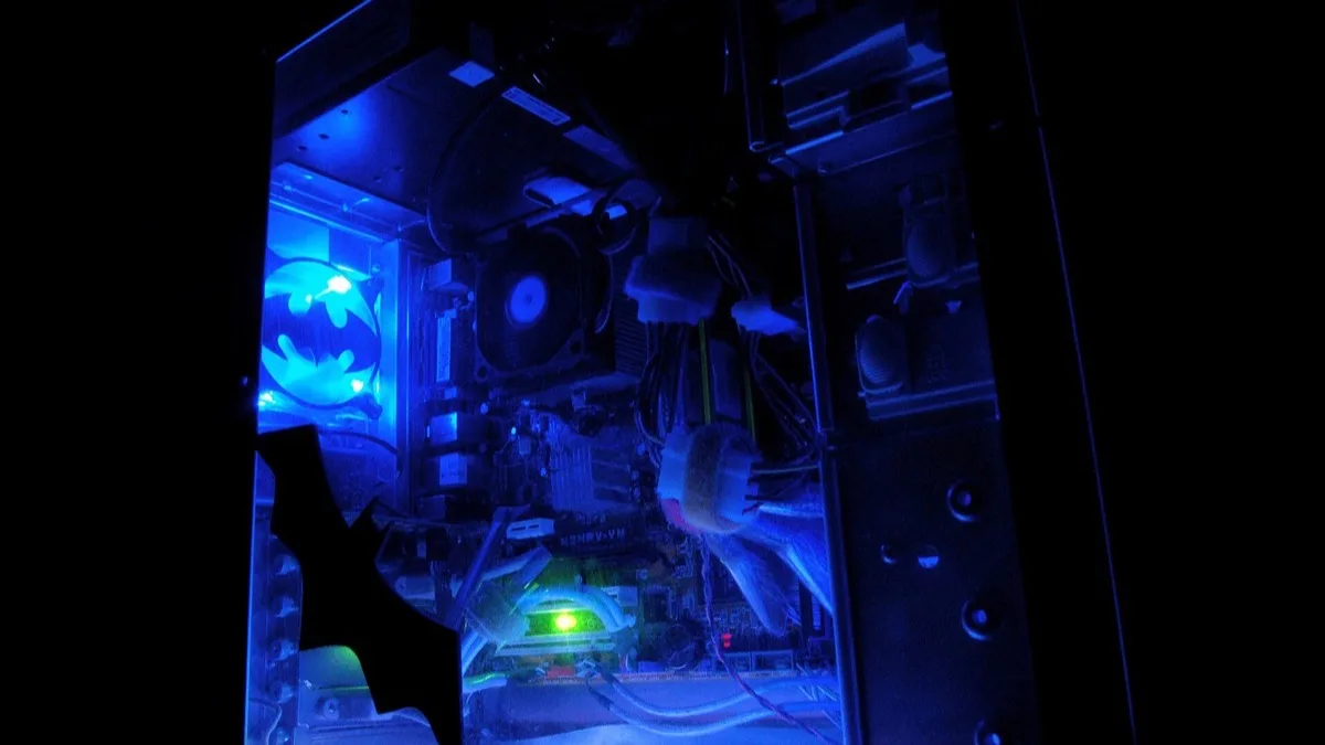 The blue-lit interior of a gaming PC tower, with a bat logo glowing on the case fan and cables running across the motherboard