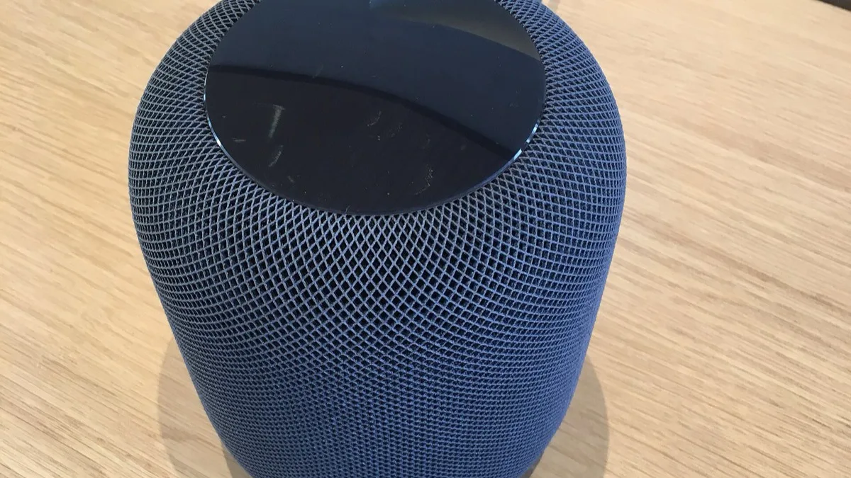 Apple HomePod smart speaker with mesh fabric covering and touch panel on top, sitting on a wooden table