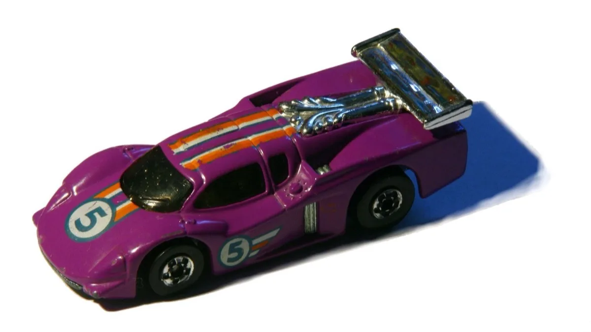 A purple Hot Wheels die-cast racing car with a chrome rear wing, photographed on a white surface