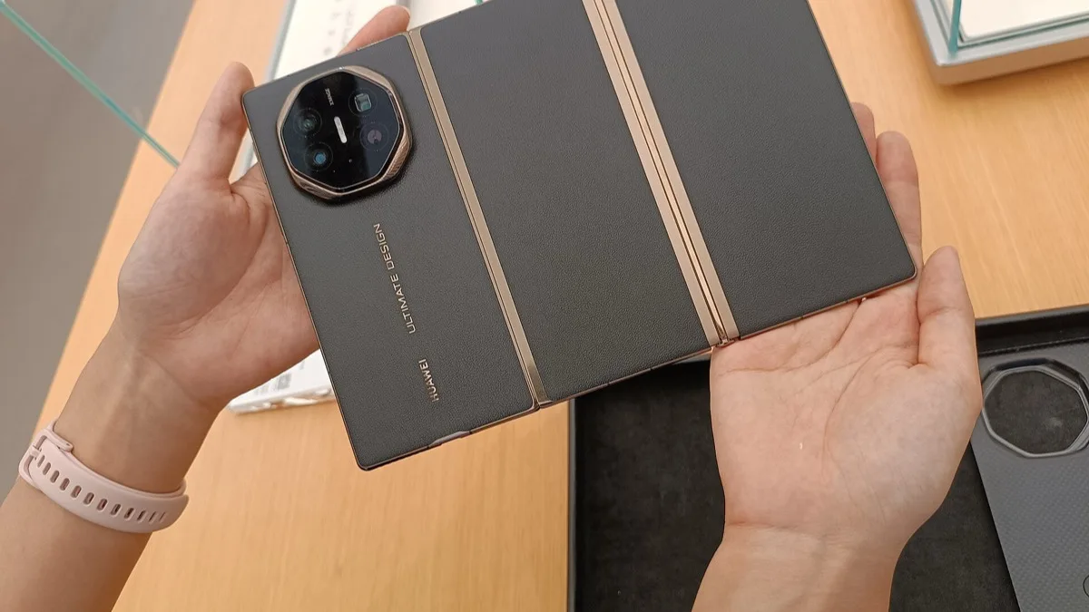 A Huawei Mate XT tri-fold phone held partly open, showing its leather-look back panel and octagonal camera module