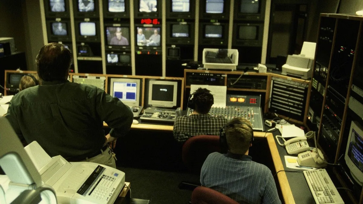 Crew members seated at a video production control desk watching a wall of camera monitors