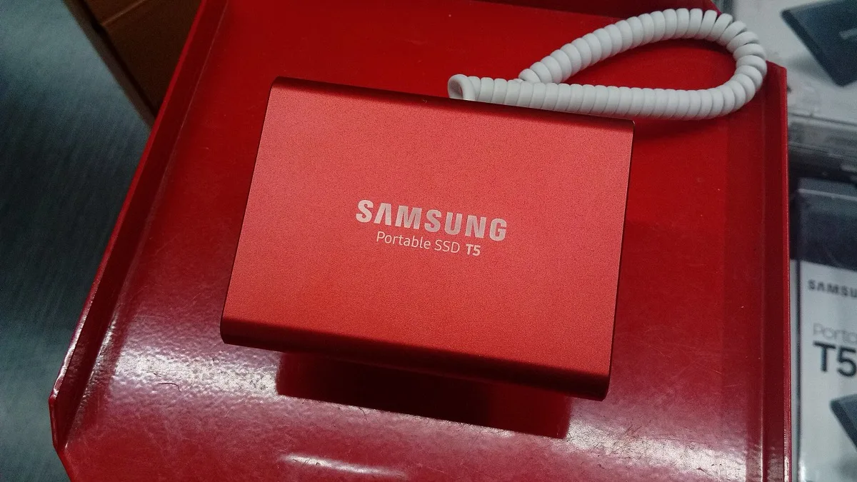 A red Samsung Portable SSD T5 external drive sitting on a red box with a coiled white cable