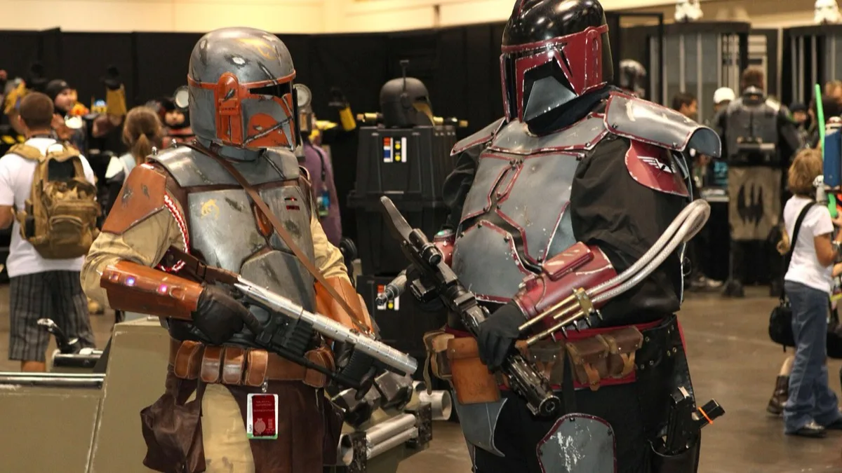 Two fans in full Mandalorian-style armour and helmets talking on the floor of a Star Wars convention