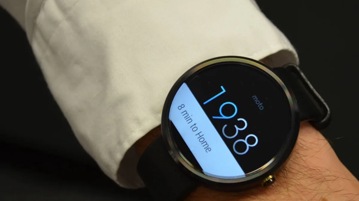 A round Motorola smartwatch on a wrist showing a watch face with the time and a travel-time notification