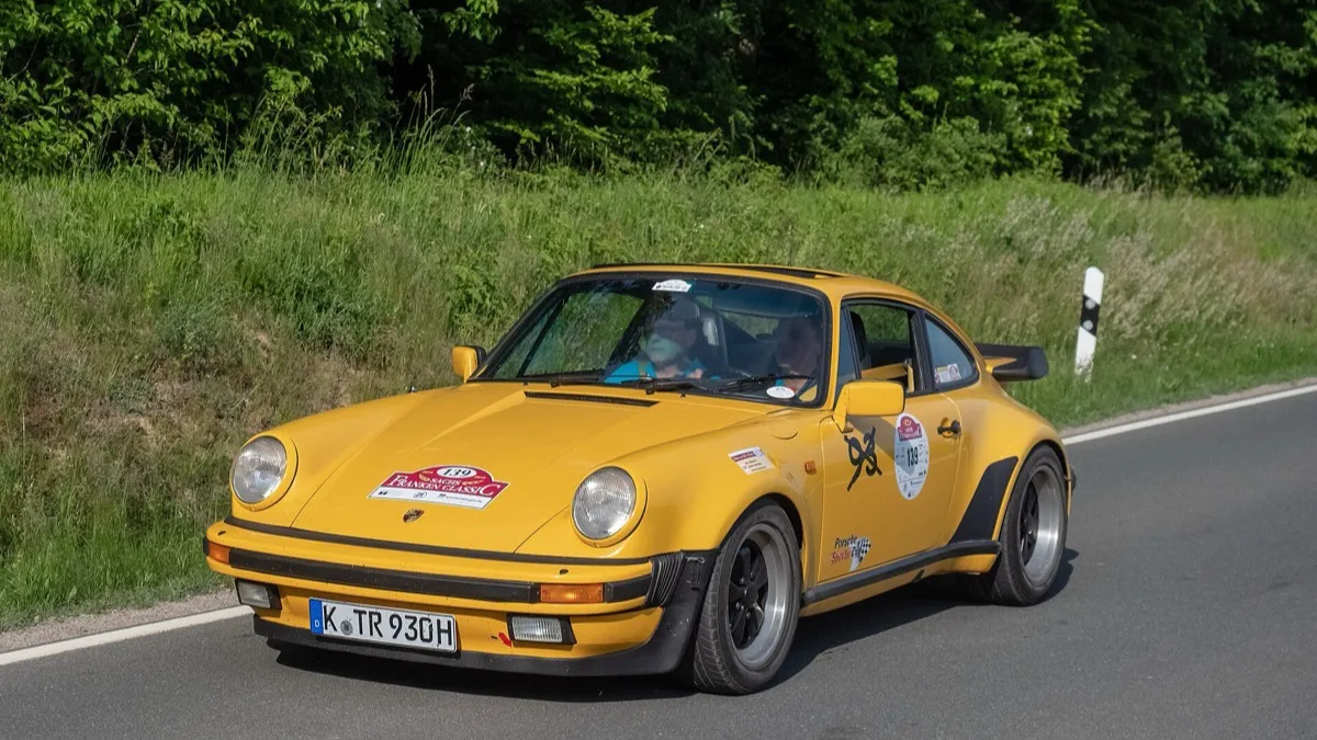A yellow 1980s Porsche 911 Turbo 930 driving along a country road during a classic car rally
