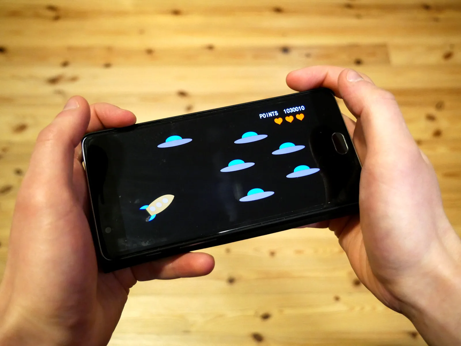 Hands holding an Android phone in landscape, playing a small arcade game that fits under 500MB offline
