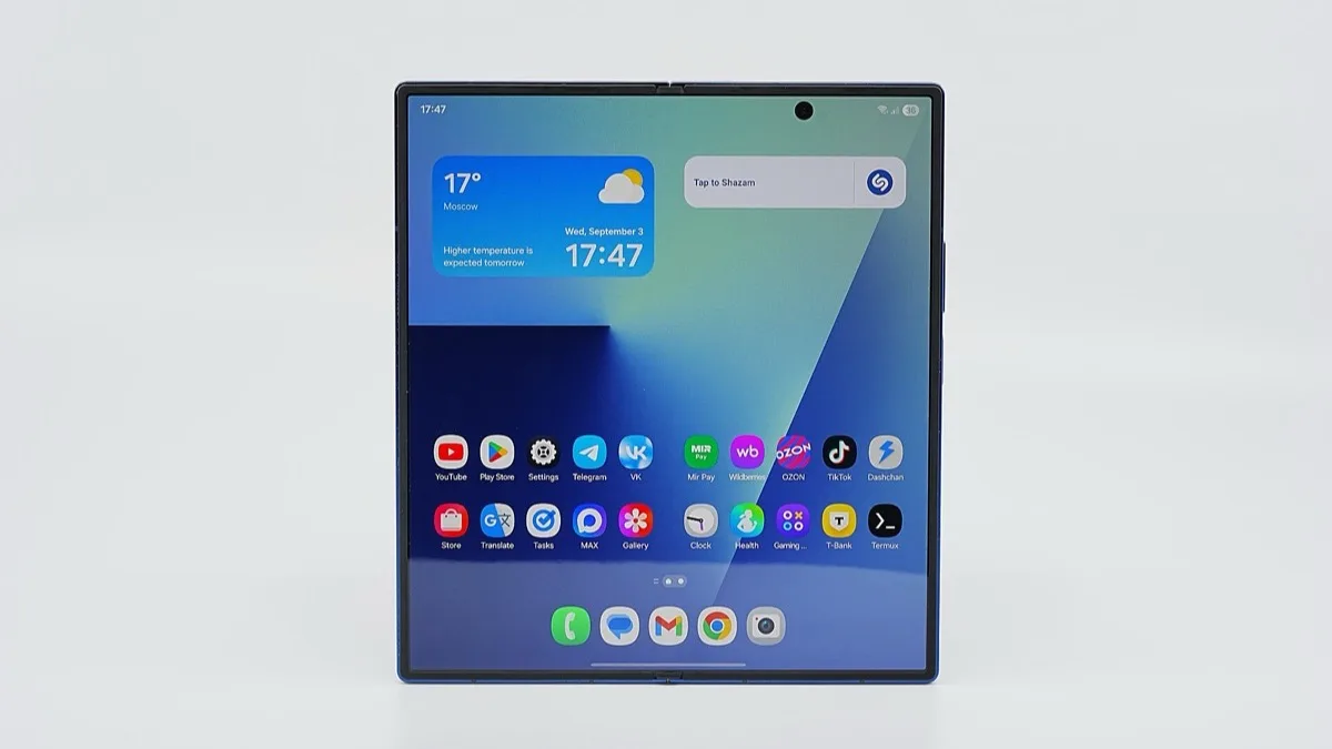 A Samsung Galaxy Z Fold7 standing unfolded on a white background, its large inner screen showing the One UI home screen with weather and clock widgets