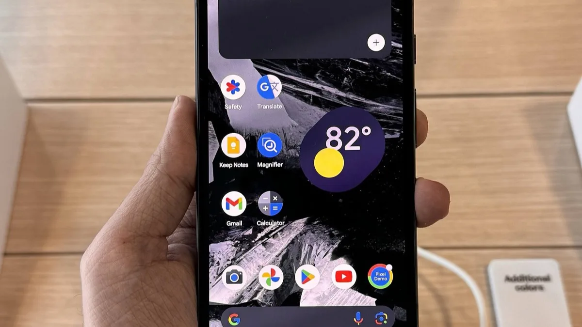 Google Pixel 8a held in a hand at a store display, showing its home screen with a weather widget