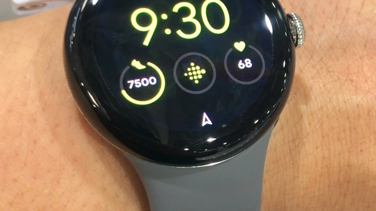 A Pixel Watch worn on a wrist, showing steps, heart rate, and a Google Maps navigation arrow on its watch face