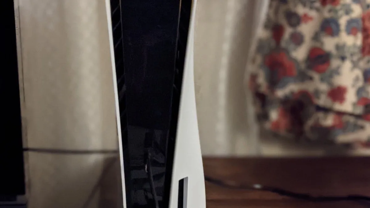 A white PlayStation 5 console standing upright on a wooden surface in a living room