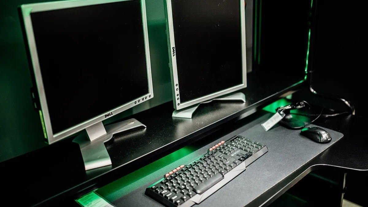 A dual-monitor PC gaming desk lit in green, with a mechanical keyboard and a wired mouse in the foreground