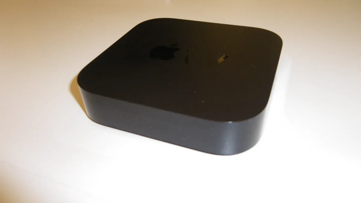 A black Apple TV streaming box sitting on a pale tabletop