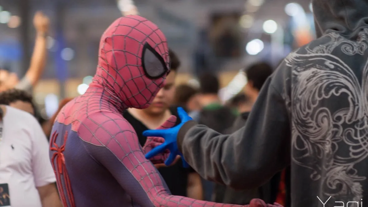 A cosplayer dressed as Spider-Man greeting another attendee in a crowded comic convention hall