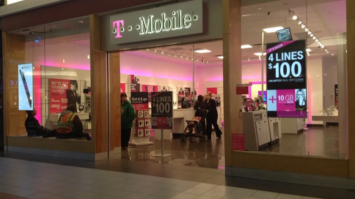 Front of a T-Mobile retail store in a shopping mall with the magenta T-Mobile sign lit above the entrance