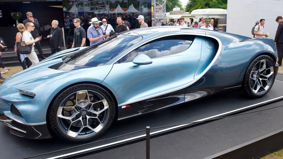 A pale blue Bugatti Tourbillon hypercar on a display stand, with visitors walking past behind it