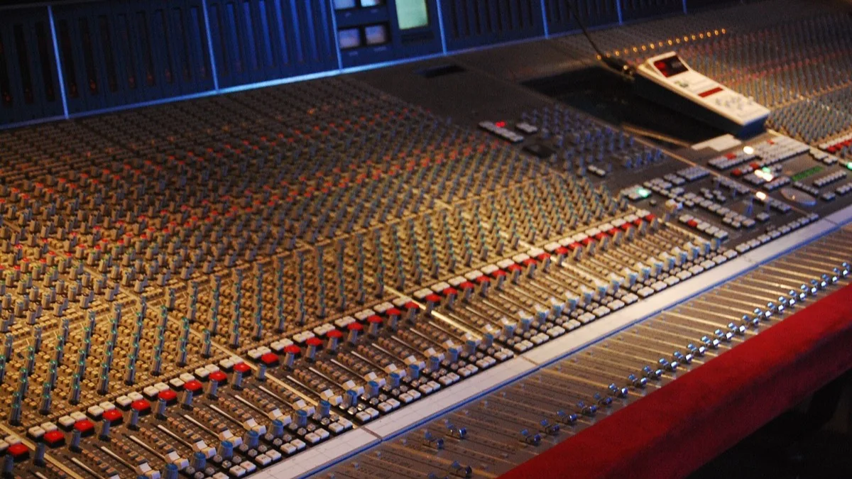 Rows of faders and coloured buttons on a large analogue mixing console in a recording studio