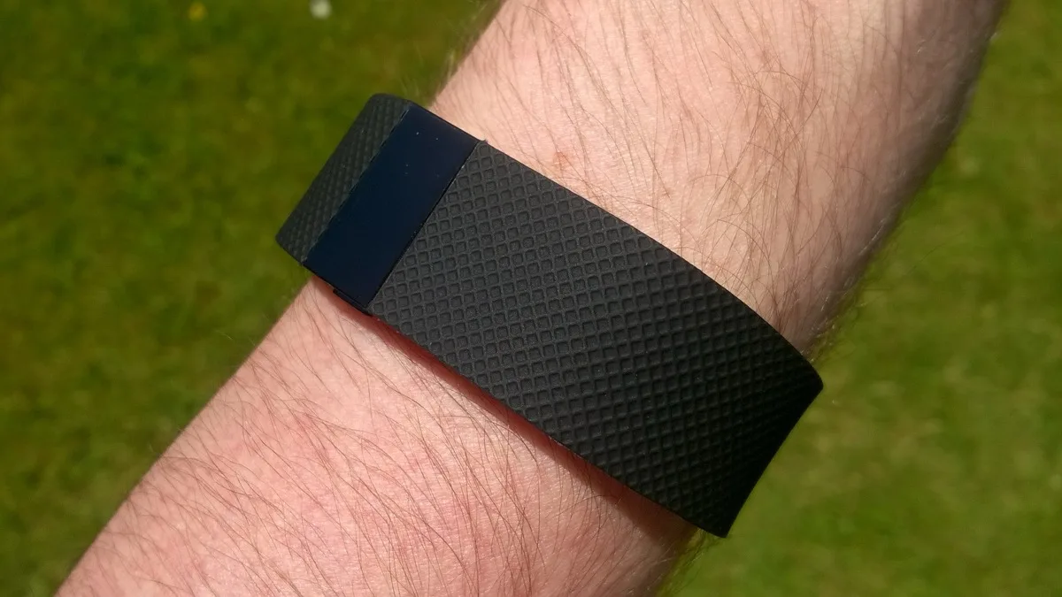 A black Fitbit Charge HR band tracker worn on a wrist, an earlier Fitbit model with a small screen