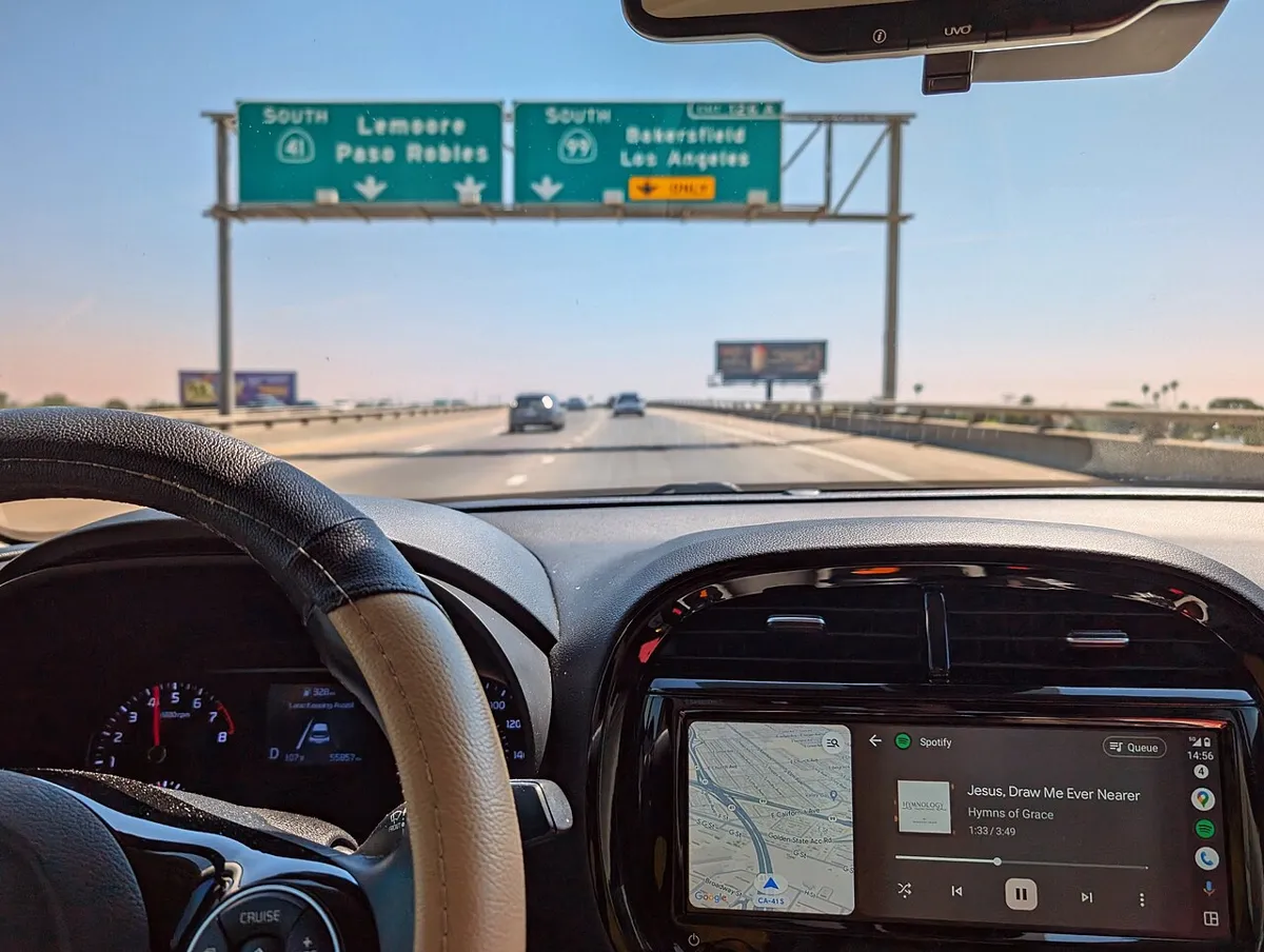 Android Auto showing Google Maps and Spotify on a car dashboard screen while driving on a California highway