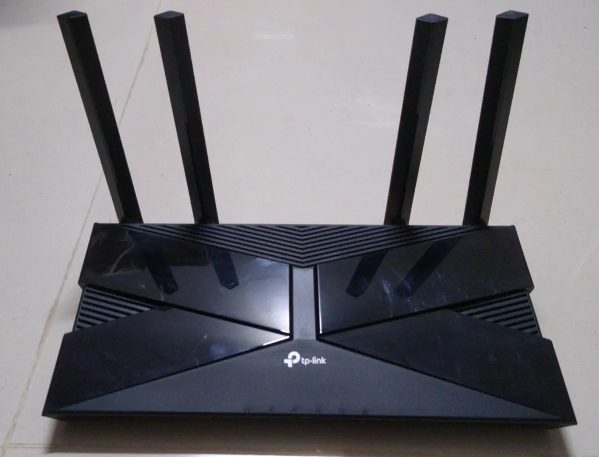 Black TP-Link AX1500 Wi-Fi 6 router with four antennas sitting on a tiled floor