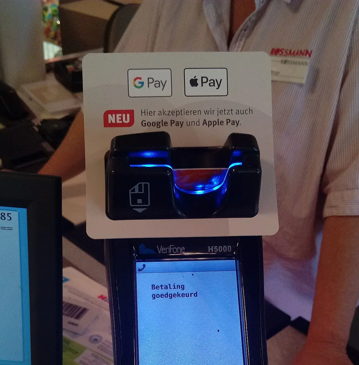 Card terminal at a store checkout with Google Pay and Apple Pay logos on a sign above the card slot