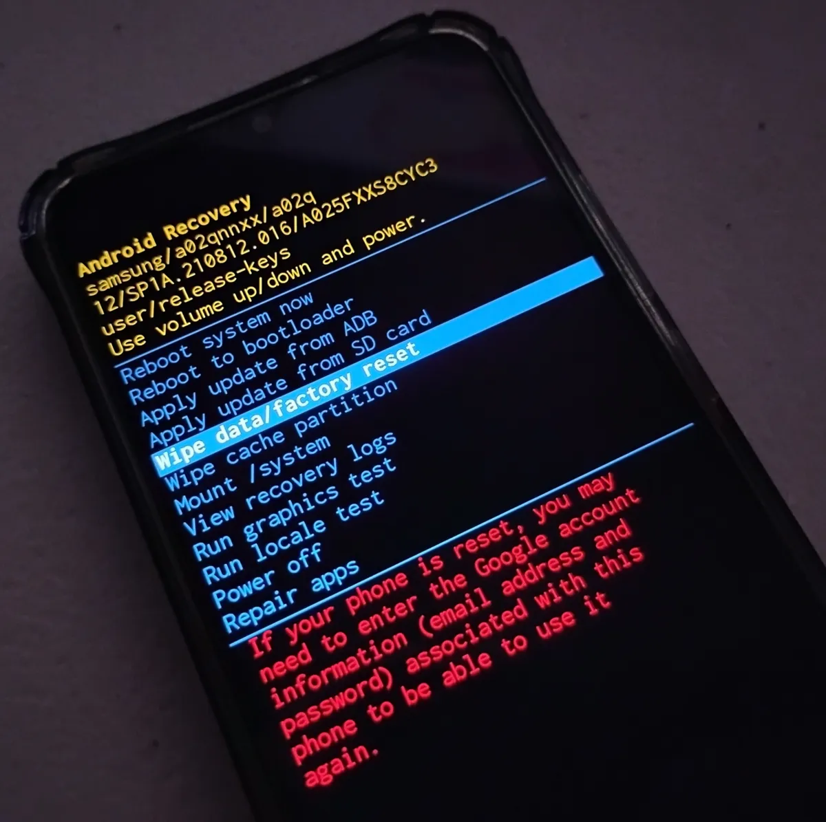 Samsung Galaxy A02s in Android Recovery with Wipe data/factory reset highlighted and a red warning about entering the Google account after a reset