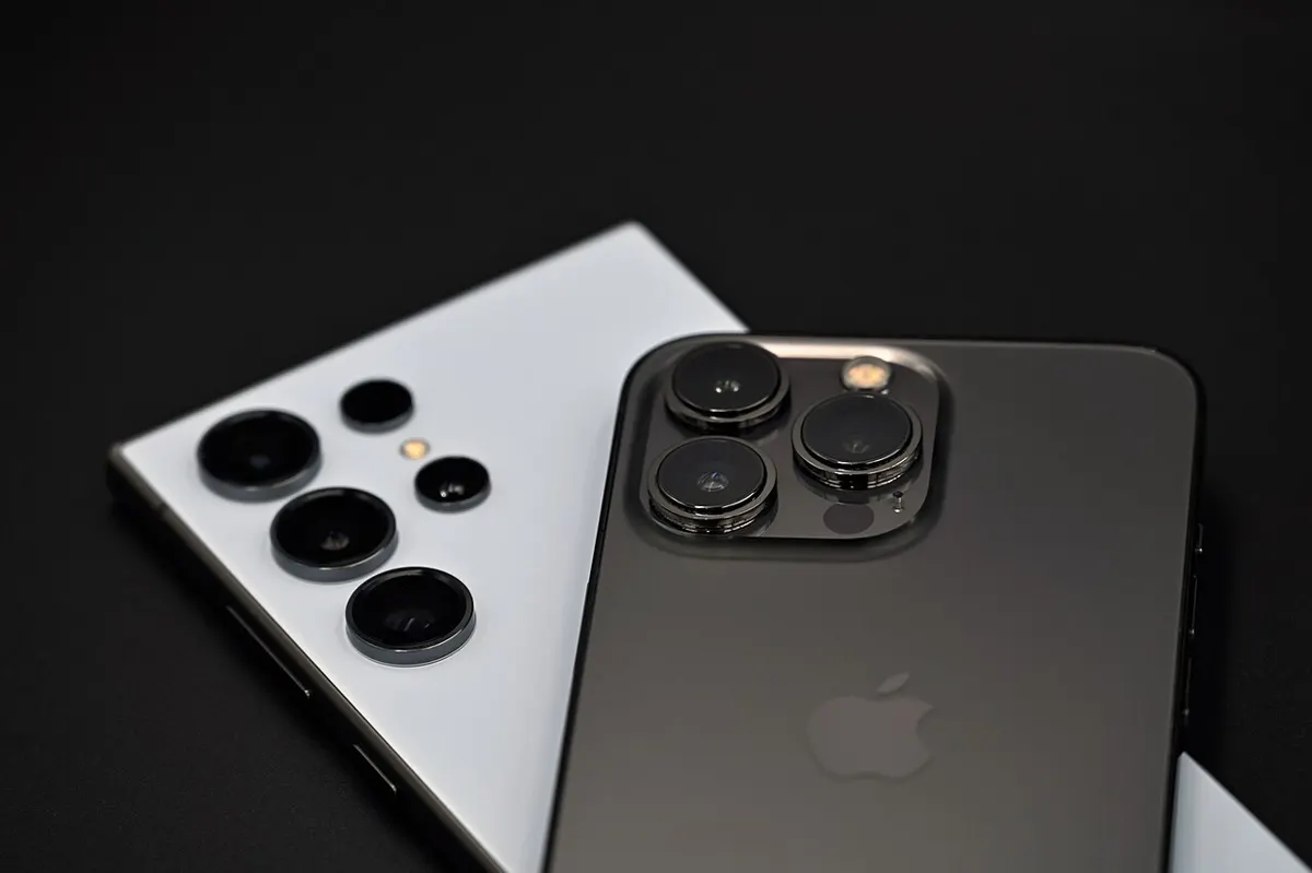 A Samsung Galaxy S24 Ultra and an iPhone 13 Pro lying back to back on a dark surface