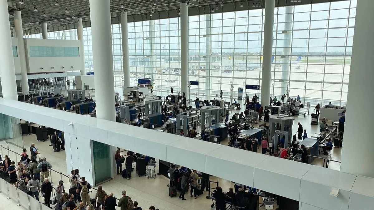 Travelers lining up at a TSA security checkpoint inside a large glass-walled US airport terminal